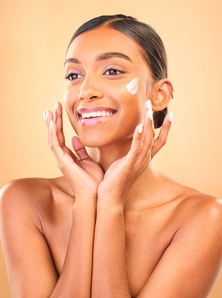 Face, skincare smile and woman with cream in studio isolated on a brown background. Dermatology cosmetics, thinking and happy Indian female model apply lotion, creme and moisturizer for healthy skin - Foto, imagen