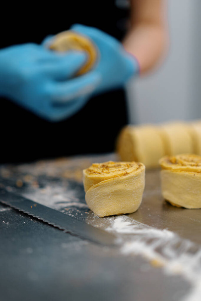 La cocina en la panadería - el proceso de hacer cinabriones, la mujer panadero corta la masa - Foto, imagen