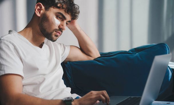 Muž na volné noze, který doma používá laptop, sedí na pohovce a dálkově pracuje na online projektu. Internetová technologie. Spokojený člověk. Životní styl lidí - Fotografie, Obrázek