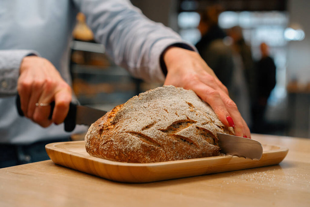 bakery - woman baker cuts freshly baked dark bread - Photo, Image