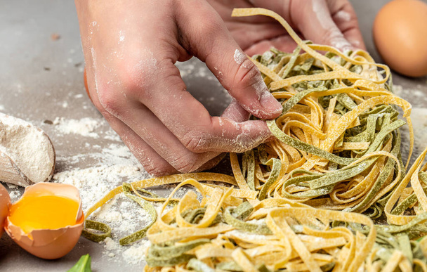 Свежая итальянская сырая домашняя паста. Руки делают макароны тальятелле. Сырая домашняя паста из шпината. - Фото, изображение