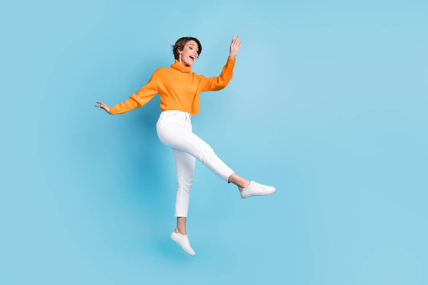 Full body photo of attractive young woman jump dance enjoy lightness elegant dressed stylish orange look isolated on blue color background. - 写真・画像