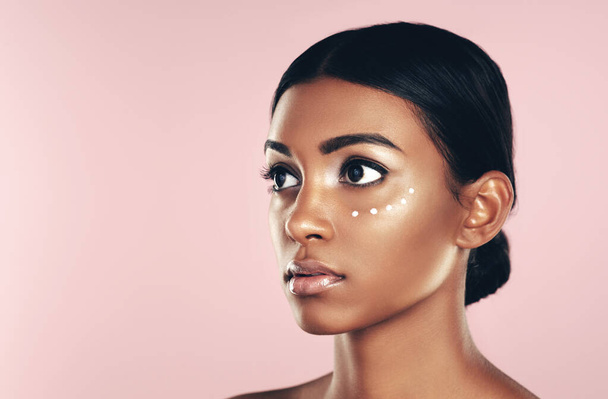 Doing some maintenance on her complexion. Studio shot of a beautiful young woman posing with moisturizer on her face against a pink background - Photo, Image