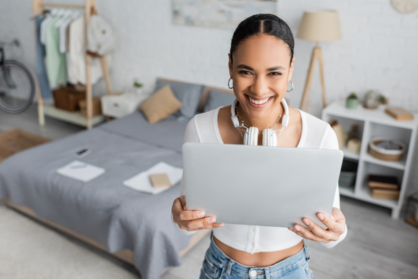 overhead view of cheerful african american student with wireless headphones on neck using laptop in modern bedroom  - Foto, Imagem