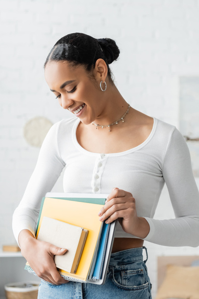 Cheerful african american student looking at notebooks at home  - Foto, Imagem