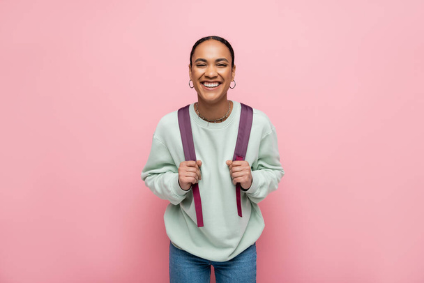 Smiling african american student holding backpack isolated on pink  - Fotografie, Obrázek
