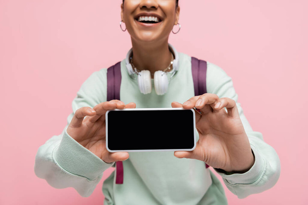 обрезанный вид на веселую африканскую американку, держащую смартфон с пустым экраном, изолированным на розовом  - Фото, изображение