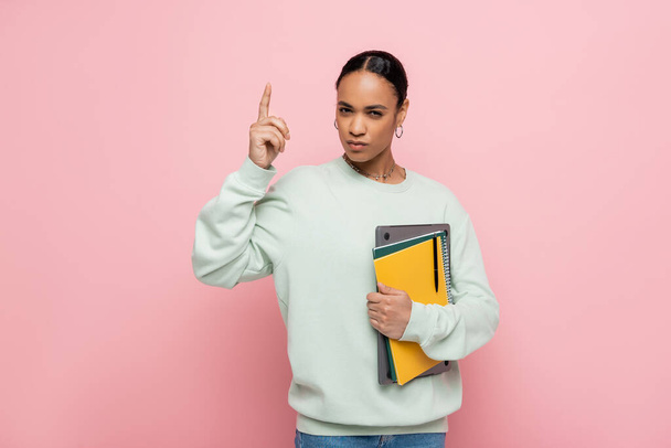 smart african american student holding laptop and notebooks while having idea isolated on pink  - Photo, Image