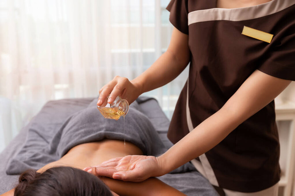 Spa therapist applying treatment oil on young woman back at salon spa. - Fotó, kép