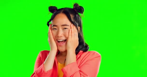 Zöld vászon és kezek az ázsiai nő arcán a stúdióban, sokkoló és boldog álarcos háttérrel. Jó hír, portré és gen z lány mosoly eladó, kedvezmény vagy divat promóció, míg elszigetelt. - Felvétel, videó