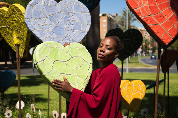 Молода і красива афро-американська жінка обіймає серця різних розмірів і кольорів в парку. Валентинів день - Фото, зображення