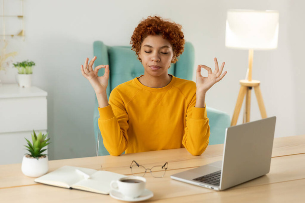 No stress keep calm. Mindful african businesswoman practices breathing exercises at home office. Peaceful young woman at workplace enjoy yoga eyes closed hands in chin mudra gesture. Office meditation - Фото, зображення