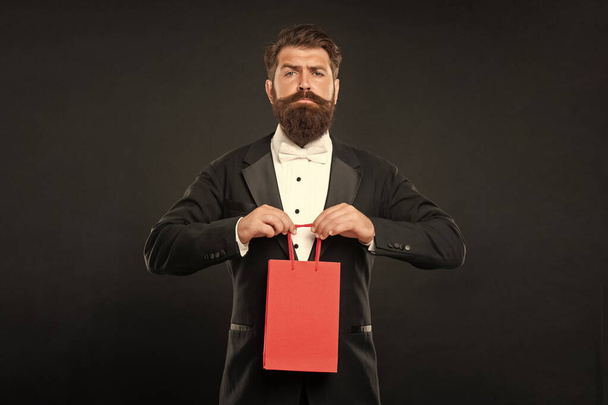 serious man in tuxedo bow tie formalwear on black background with business reward in shopping bag. occasion greeting. copy space. - Foto, Imagen