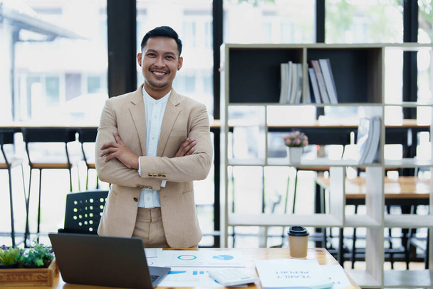 Porträt eines männlichen Geschäftsinhabers, der ein fröhlich lächelndes Gesicht zeigt, als er sein Geschäft erfolgreich mit Computern und Haushaltsdokumenten bei der Arbeit investiert hat. - Foto, Bild