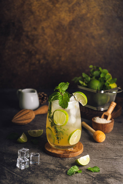 Iced Mojito cocktail long rum drink with fresh mint, fresh thyme, lime juice, cane sugar and soda on dark abstract background. Summer iced beverage and cocktail - Φωτογραφία, εικόνα