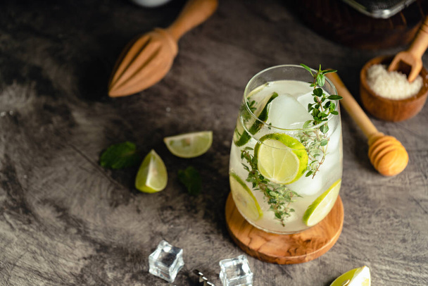 Iced Mojito cocktail long rum drink with fresh mint, fresh thyme, lime juice, cane sugar and soda on dark abstract background. Summer iced beverage and cocktail - Photo, image