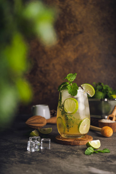 Iced Mojito cocktail long rum drink with fresh mint, fresh thyme, lime juice, cane sugar and soda on dark abstract background. Summer iced beverage and cocktail - Fotoğraf, Görsel