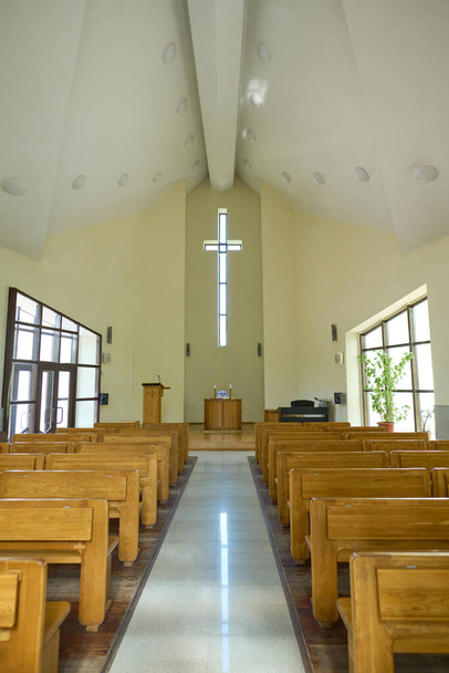 Interior da igreja católica moderna com duas fileiras de bancos de madeira para paroquianos e corredor longo levando ao púlpito com cruz acima - Foto, Imagem