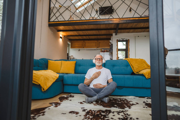 Egy férfi vezető kaukázusi férfi szeme csukva vezetett edzés jóga vagy meditáció, miközben otthon ül a fejhallgató öngondoskodó gyakorlat valós emberek jólét belső béke és egyensúly koncepció - Fotó, kép
