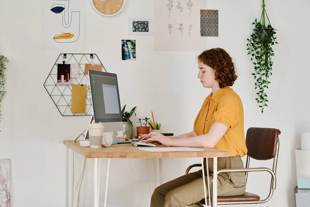 Nuori, vakava naispuolinen freelancer tai webdesigner, joka keskittyy työhön uuden verkkosivuston luomisessa istuessaan tietokoneen ääressä - Valokuva, kuva