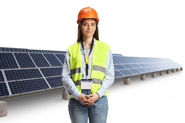Young female engineer with a safety vest and hardhat standing in front of a solar panel field isolated on white background - Foto, Imagem