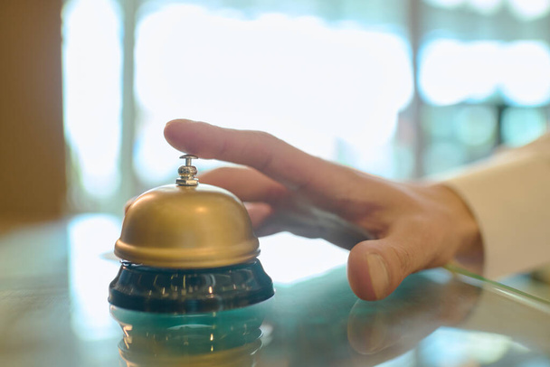 若い男性旅行者の手は、ホテルに到着した後にカウンターに立っている間、受付を呼び出すために鐘の上にボタンを押すつもりです。 - 写真・画像
