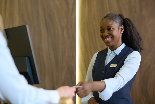 Onnellinen nuori musta nainen yhtenäinen kulkee passi tai avainkortti mies matkailija over counter rekisteröinnin jälkeen hänen henkilötietonsa - Valokuva, kuva