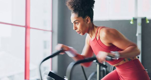 Exercise bike, cardio and girl cycling for sports fitness, athlete marathon training or high energy body workout. Gym performance motivation, wellness mindset and black woman riding bicycle machine. - Photo, Image