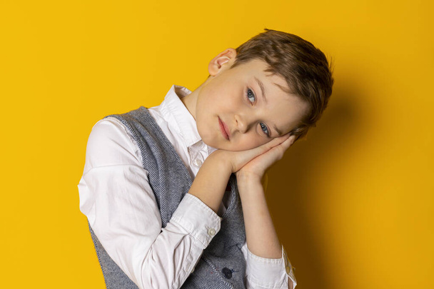 Portrait of An adorable little boy in gray vest and white shirt, neatly dressed. sleep gesture. Isolated on yellow background. - Foto, imagen