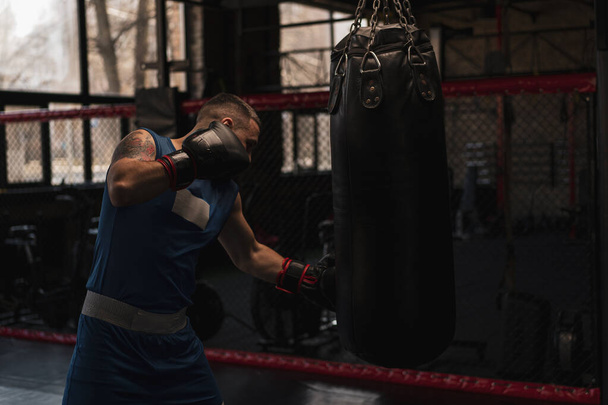Boxe gymnase un boxeur entraîne ses coups frapper sac de boxe - Photo, image