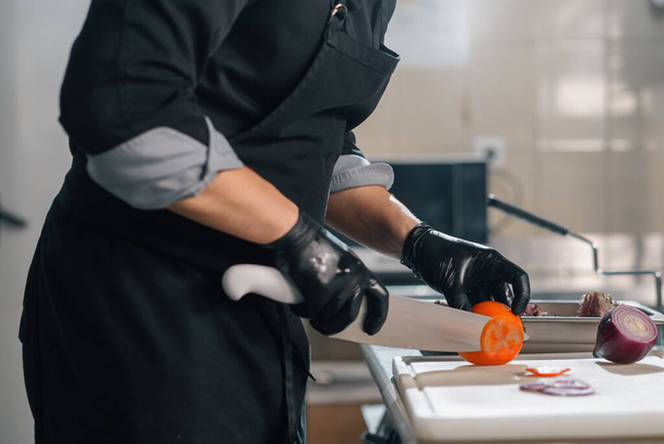 professional kitchen in hotel restaurant chef with kitchen knife cuts vegetables burger - Φωτογραφία, εικόνα