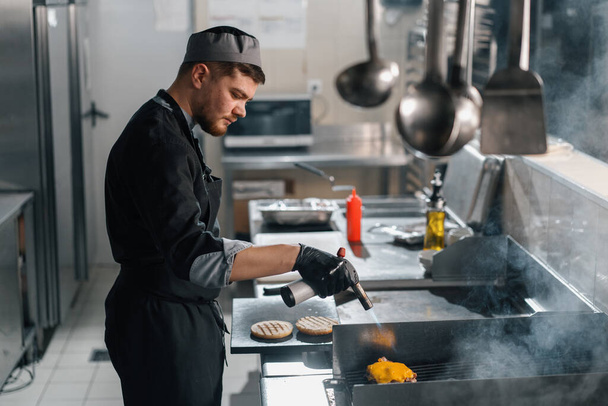professional kitchen in hotel restaurant chef with kitchen torch browning cheese burger patty - Foto, Imagen