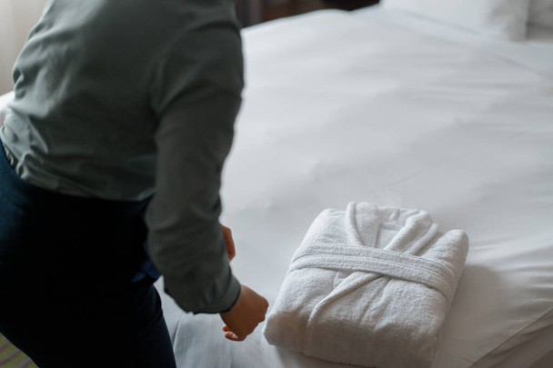 Housekeeper in uniform is folding white coat preparing luxury hotel room guests cleaning and travel concept - Photo, Image