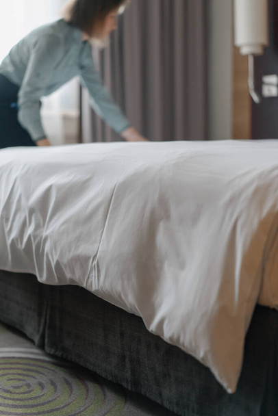 Gospodyni w mundurze tworzy łóżko przygotowujące luksusowy pokój hotelowy dla gości sprzątających i podróżujących - Zdjęcie, obraz