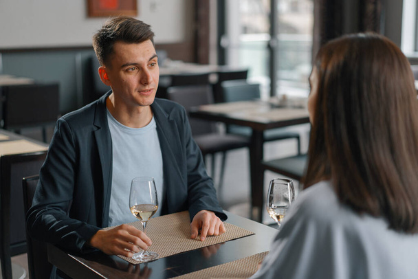 Uma data em um restaurante do hotel, um homem e uma mulher bebem vinho branco em copos o rosto de homem sério - Foto, Imagem