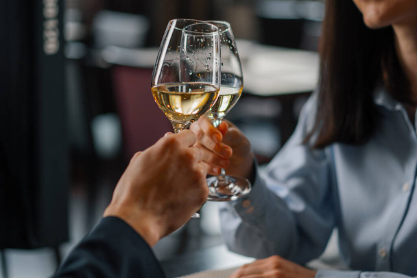 Una cita en un hotel restaurante hombre y una mujer beber vino blanco en vasos de cerca - Foto, imagen