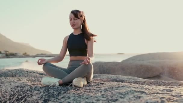 Meditation, peace and yoga with woman at beach for spiritual, mindfulness and fitness. Wellness, freedom and windy with girl breathing on rocks in nature for faith, summer break and calm mindset. - Materiaali, video