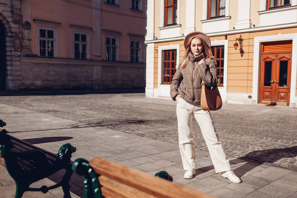 Full body portrait of stylish young woman walking on city street wearing stylish hat and jacket carrying handbag. Spring fashion. Beige white and brown clothes and accessories. Space - Foto, Imagen
