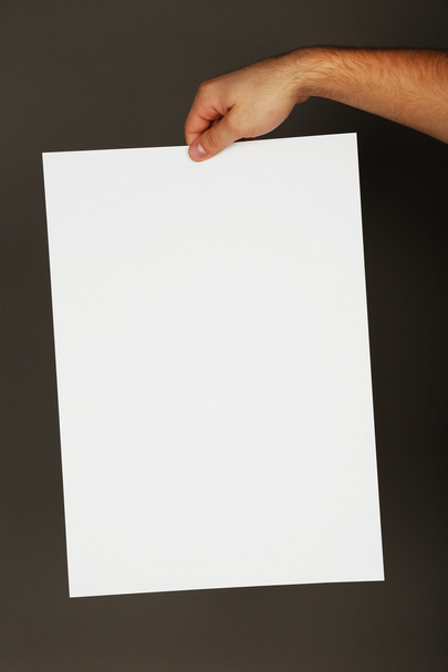Blank sheet of paper in male hand on dark background - Foto, Imagen