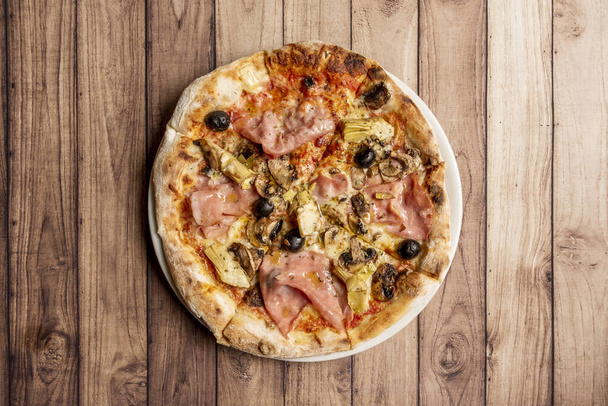 A pizza capricciosa egy olasz ételekből készült pizza, mozzarella sajttal, sütőben sült olasz sonkával, articsókával, paradicsommal és ehető gombával, ami általában gomba. - Fotó, kép