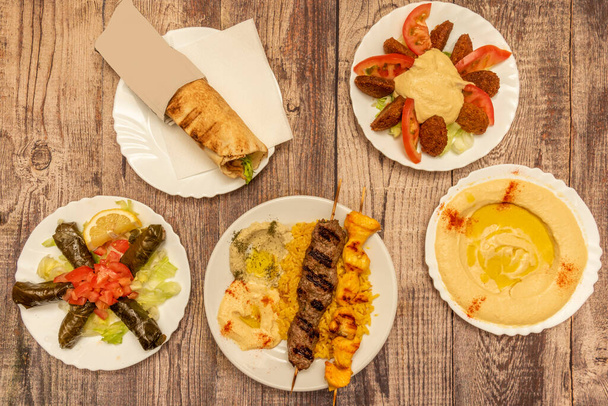 Set di ottimi piatti arabi e mediorientali con vino sarma, shawarma, spiedini di carne alla griglia, hummus con olio e paprika, falafel con insalata sulla tavola di legno - Foto, immagini