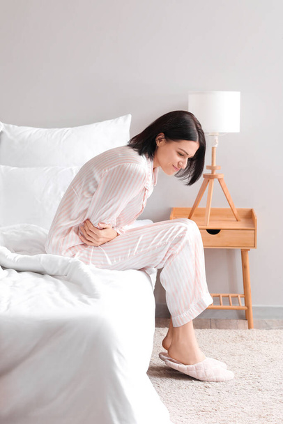Young woman suffering from menstrual cramps in bedroom - Foto, imagen