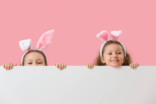 Dziewczynki w króliczych uszach z pustym plakatem na różowym tle. Wielkanoc - Zdjęcie, obraz