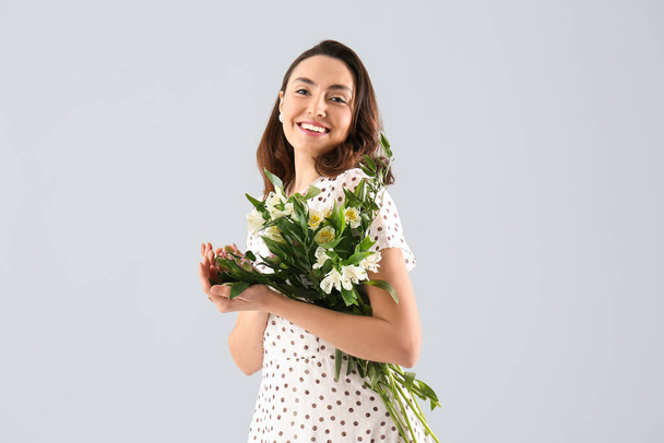 Mladá žena v šatech s alstroemeria květiny na šedém pozadí - Fotografie, Obrázek