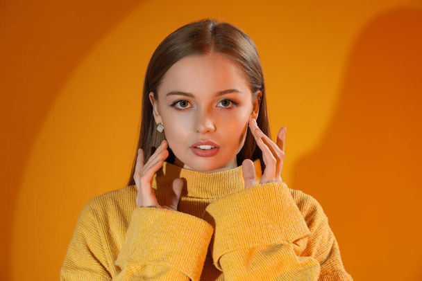 Fashionable young woman in knitted sweater on orange background - Foto, Imagen