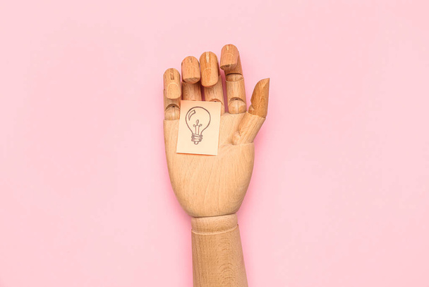 Wooden hand and sticky paper with drawn light bulb on pink background. Insight concept - Photo, Image