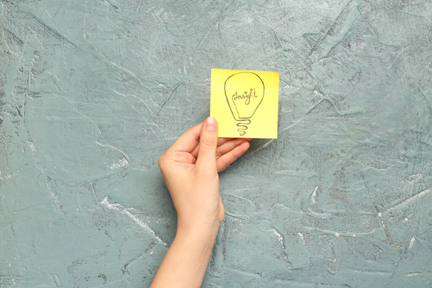 Woman holding sticky paper with drawn light bulb on grunge background. Insight concept - Valokuva, kuva