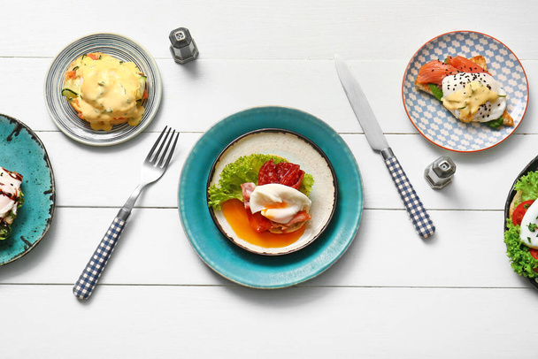 Složení s talíři z různých vajec Benedikt na bílém dřevěném stole - Fotografie, Obrázek