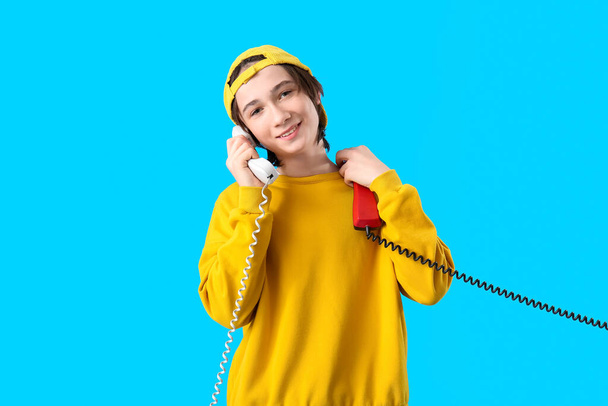 Cool teenage boy with phone receivers on blue background - Photo, Image
