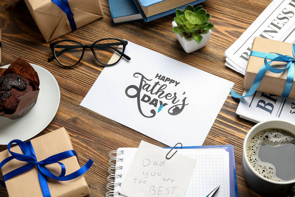 Kaart met tekst HAPPY FATHER 'S DAY, bril, muffin, kopje koffie en geschenken op houten ondergrond, close-up - Foto, afbeelding